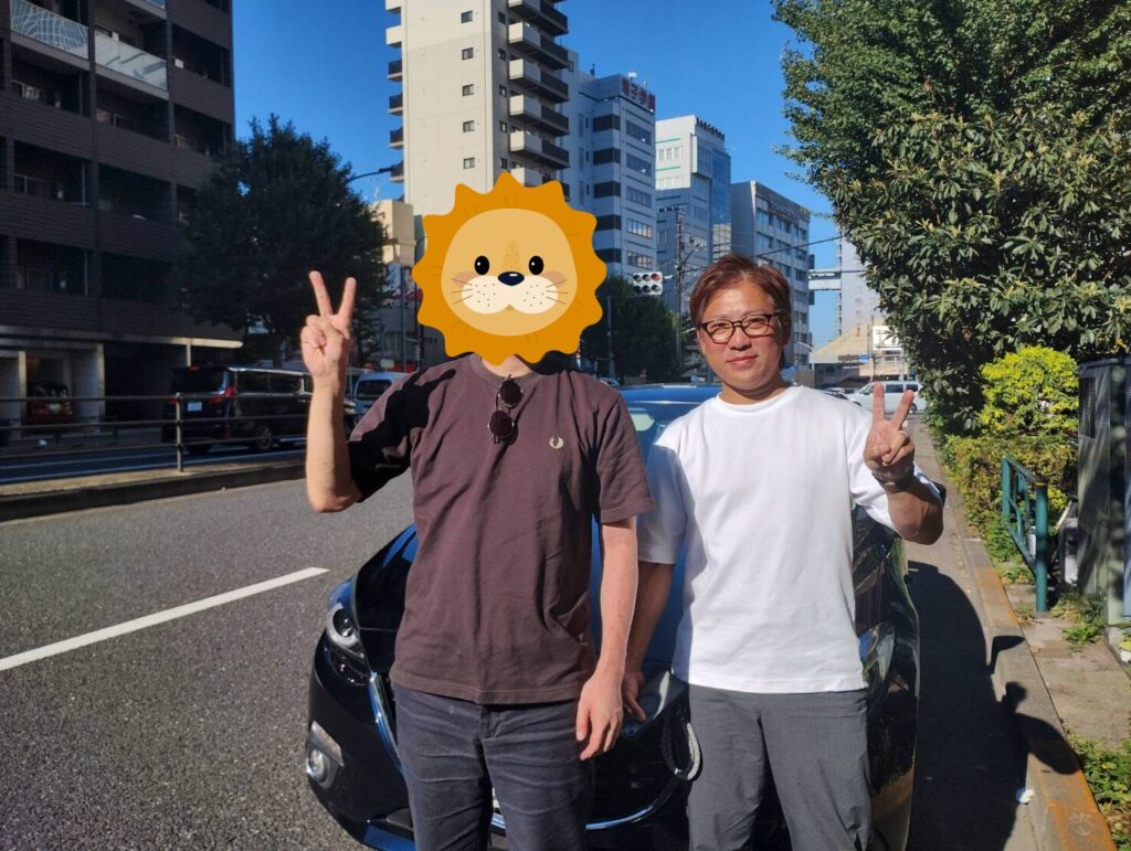 ペーパードライバー講習を終えた受講者とインストラクターが講習車の前でピースサイン（東京都内）