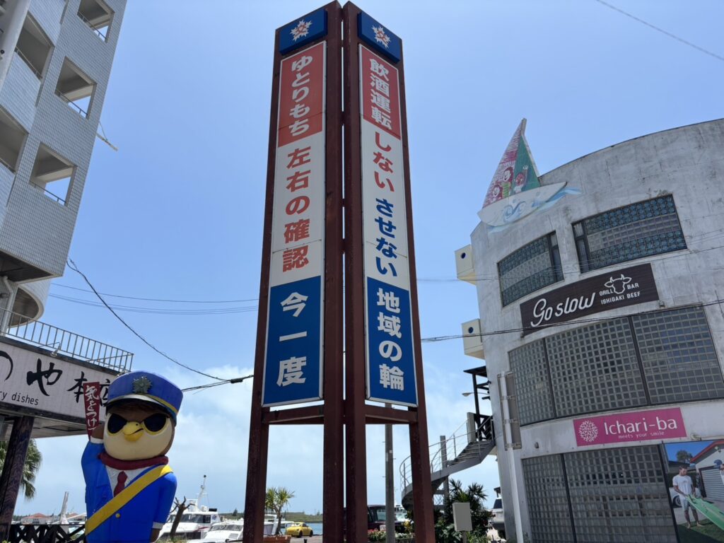 石垣島 交通安全看板 飲酒運転防止と左右確認 石垣島の市街地にある交通安全看板と警察キャラクター像。飲酒運転防止や左右確認を呼びかけている様子。