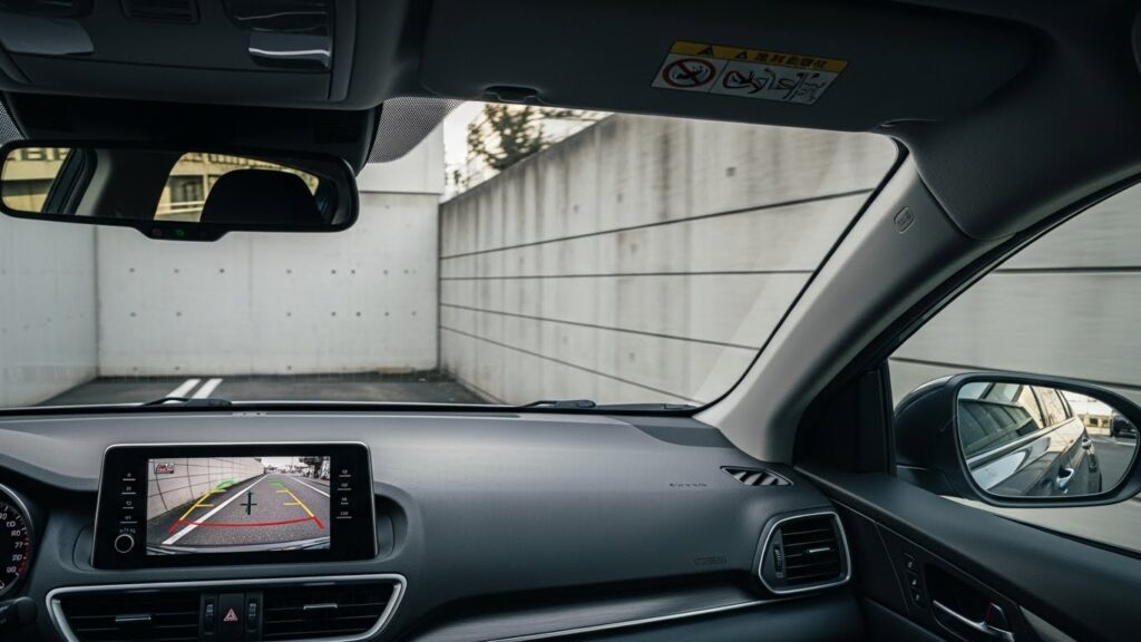 バックモニターに映る後方の壁を確認しながら後退する車内視点。バック操作が苦手な人が混乱しやすい状況を示すイメージ。